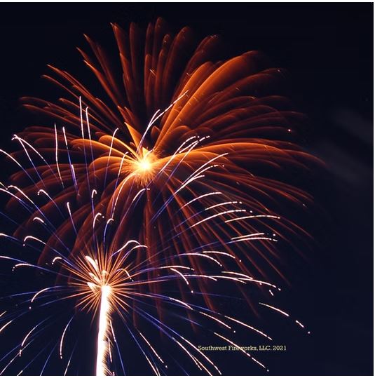Orange palm shell break above a bright gold spider shell rising from the ground during a professional fireworks display