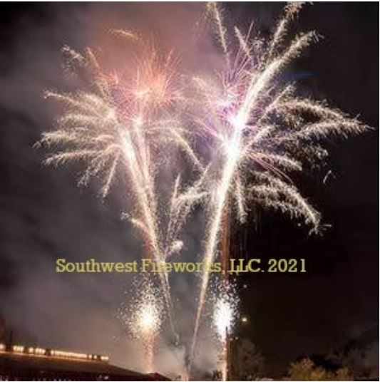 Wide view of multiple pink, gold, and white fireworks shells breaking together above a distant venue at night