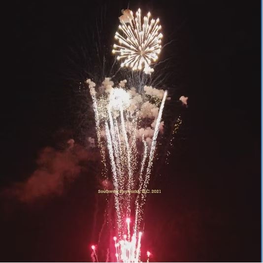 Multi-color finale with a bright gold aerial shell above dense red and white comet trails rising from ground effects