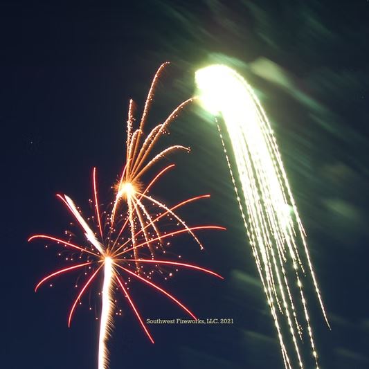 Bright gold aerial waterfall firework cascading long trails downward beside a red and orange aerial shell break