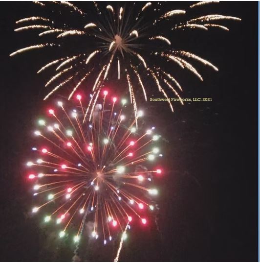 Two aerial fireworks shells breaking together — a white and gold burst above a large multi-color red, green, and blue peony with vivid pistil dots