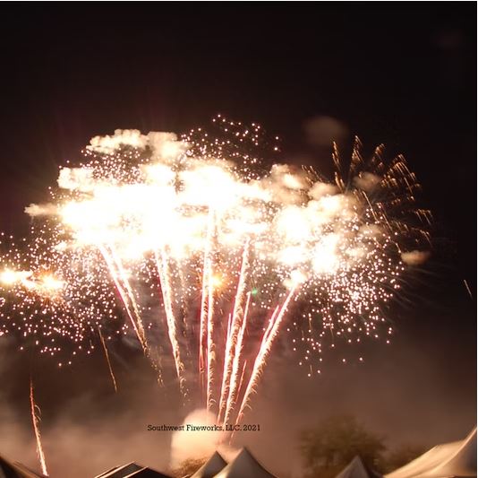Wide bright finale of layered gold and white fireworks shells and comet trails filling the sky above event tents at Skies Over Bagdad